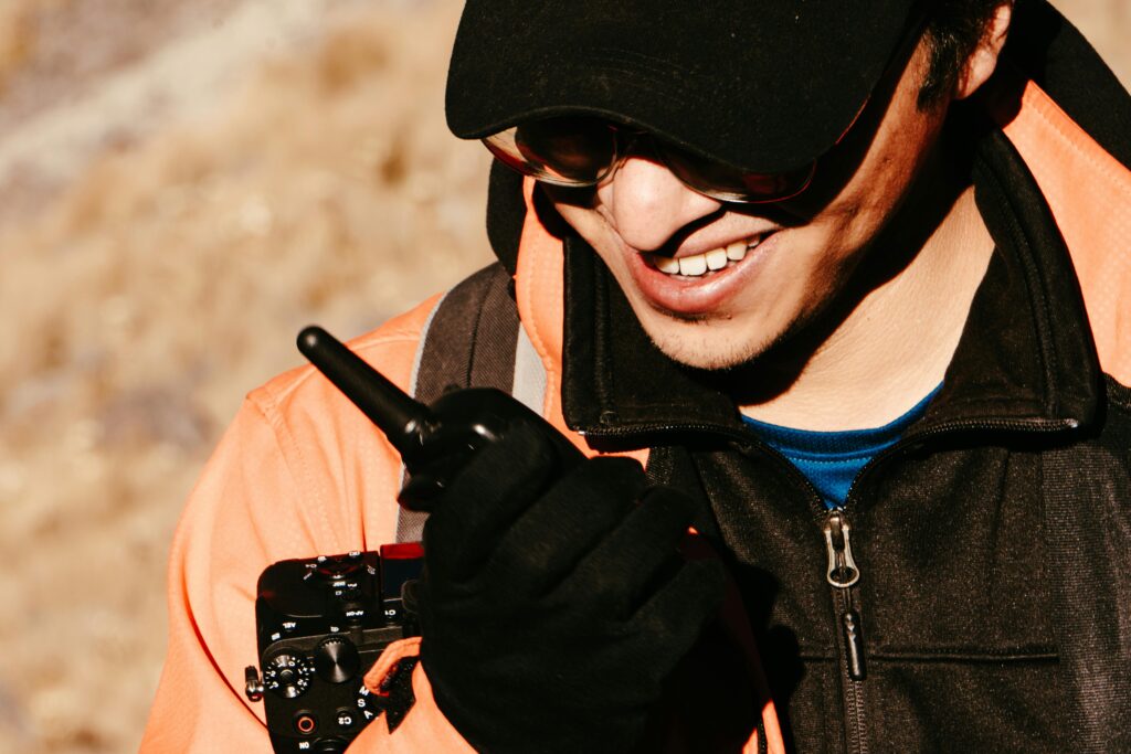 Man using a two-way radio outdoors, wearing sunglasses and an orange jacket, in Toluca de Lerdo, Mexico.