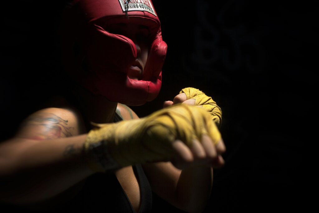 A fierce female boxer wearing protective gear during intense training in a dark setting.