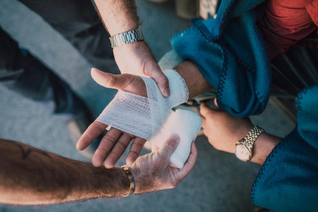 Close-up of two people bandaging an injured hand outdoors, focusing on first aid care.