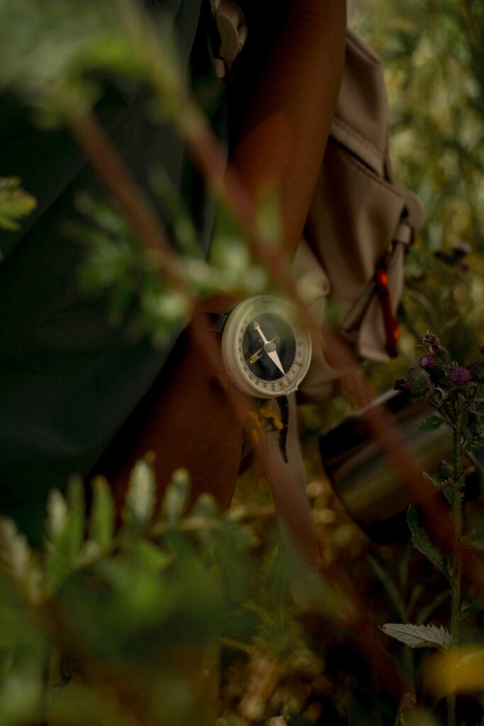 Compass held by a hiker amidst lush forest foliage, providing a sense of adventure and exploration.