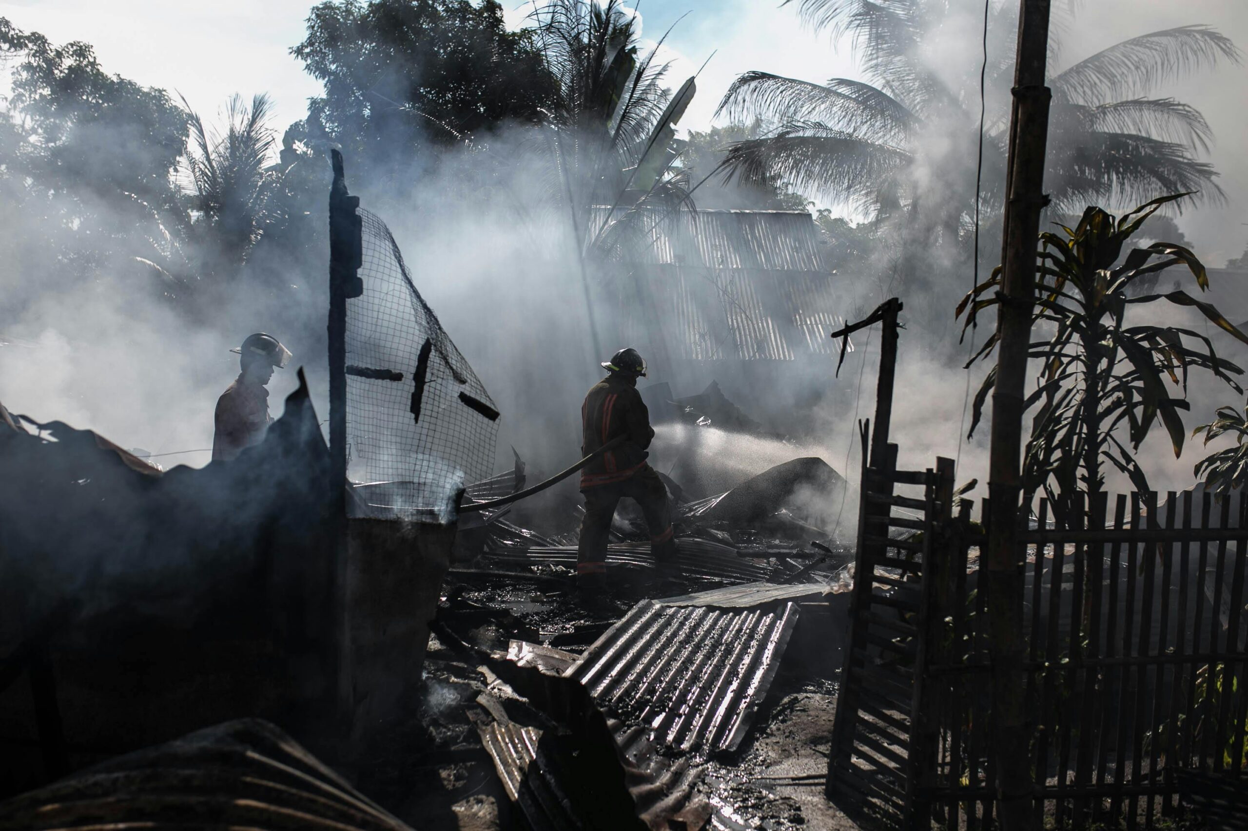 Brave firefighters battle a blaze amidst thick smoke in an outdoor setting.