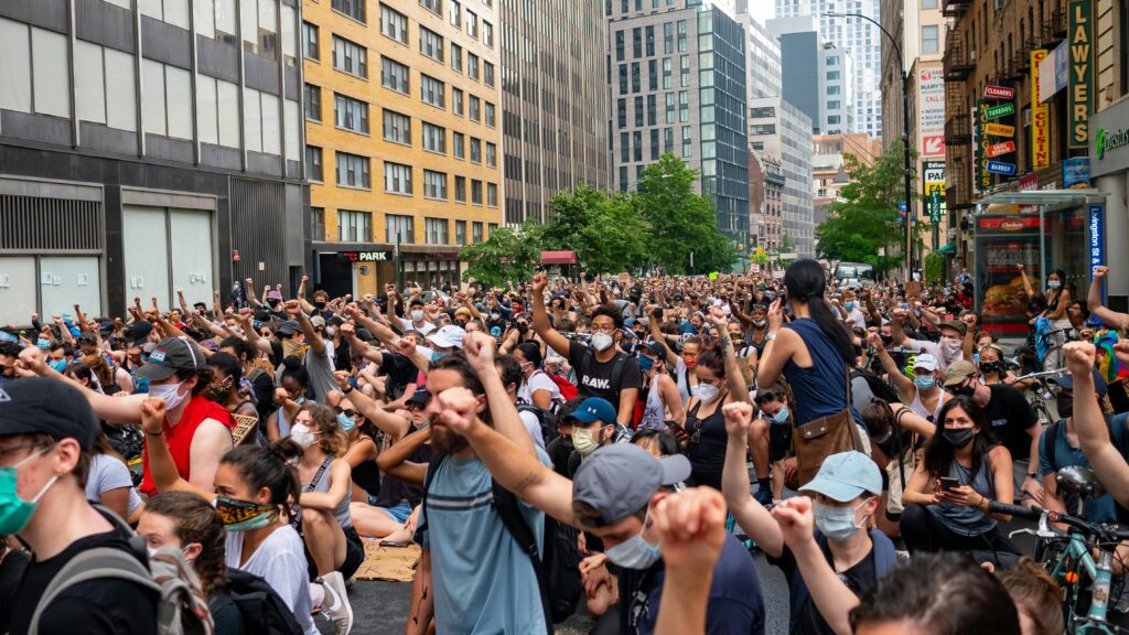 A large crowd of diverse protesters raising fists in a city street during daytime.